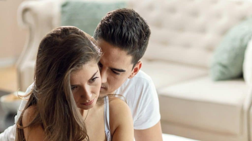 A young woman is feeling sad while her husband is embracing her.