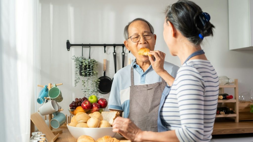 A woman feeding her old husband in the kitchen.