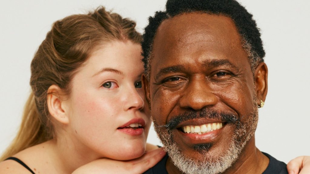An older man smiling and a young woman resting her head on his shoulders.