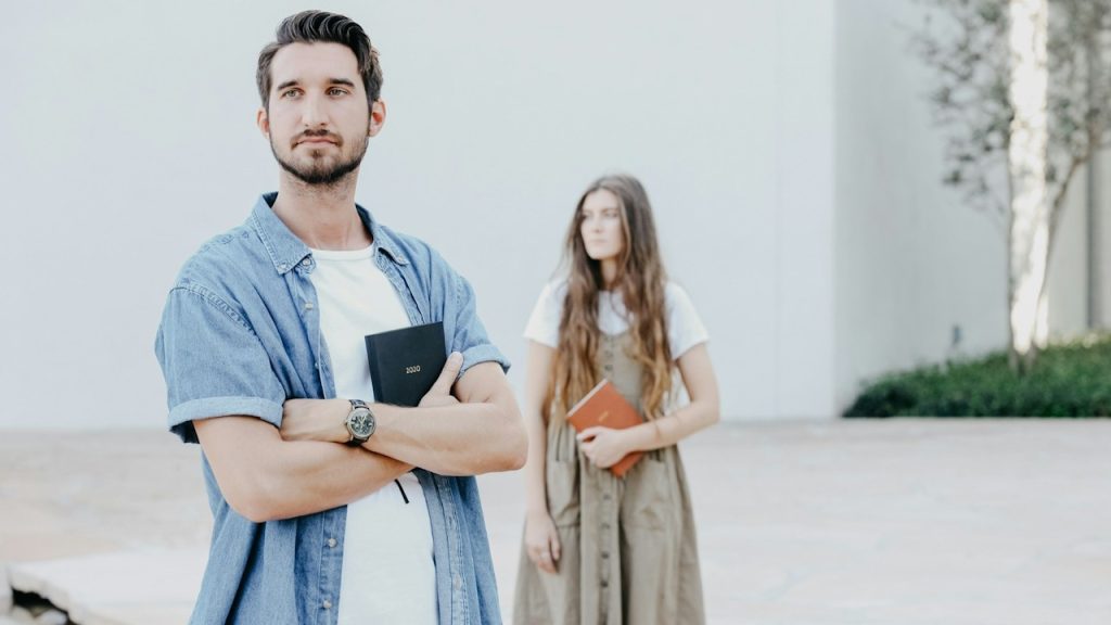 A man and a woman standing in university while holding books in their hands.