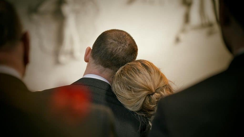 A woman resting her head on a man's shoulder, viewed from behind, in a formal setting.