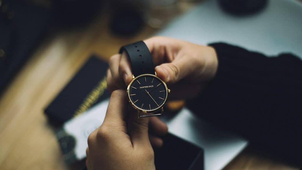 Person holding-gold-colored analog watch with a black strap.