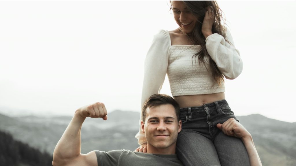 A man holding a woman on his shoulder and showing off his muscles.