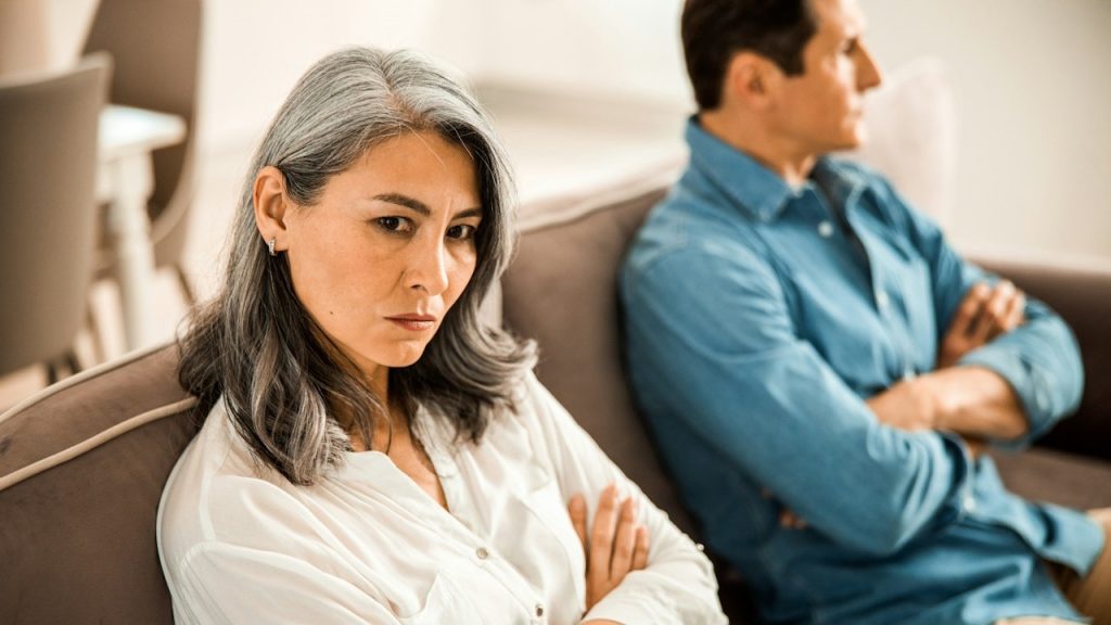 A couple sitting on a couch with their arms crossed and looking away from each other.