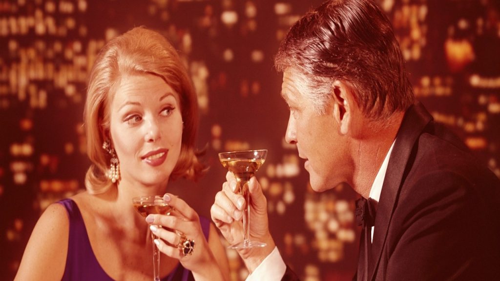 A romantic couple drinking champagne with a city skyline at night in the background.
