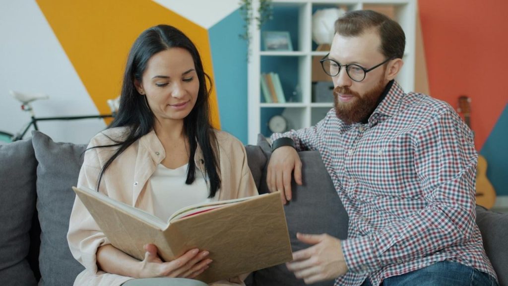 A couple sitting on a couch and looking through an album.