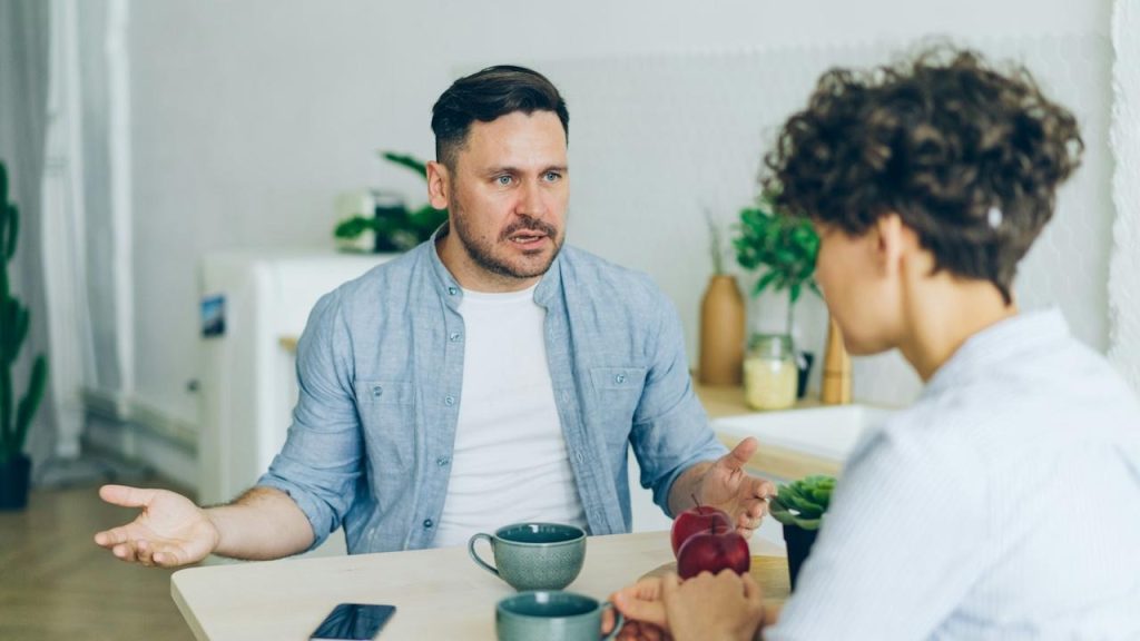 A man sitting at a table talking to a woman.