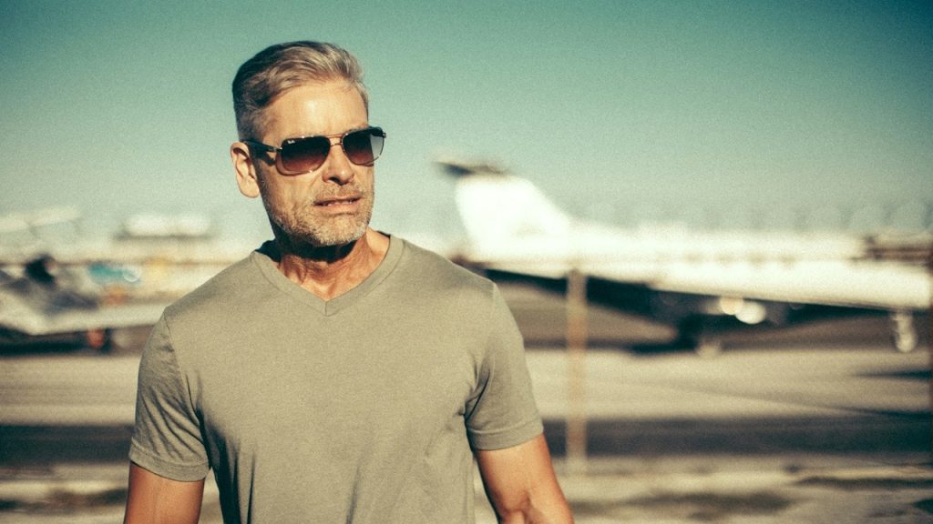 A man wearing sunglasses is walking across an airfield.