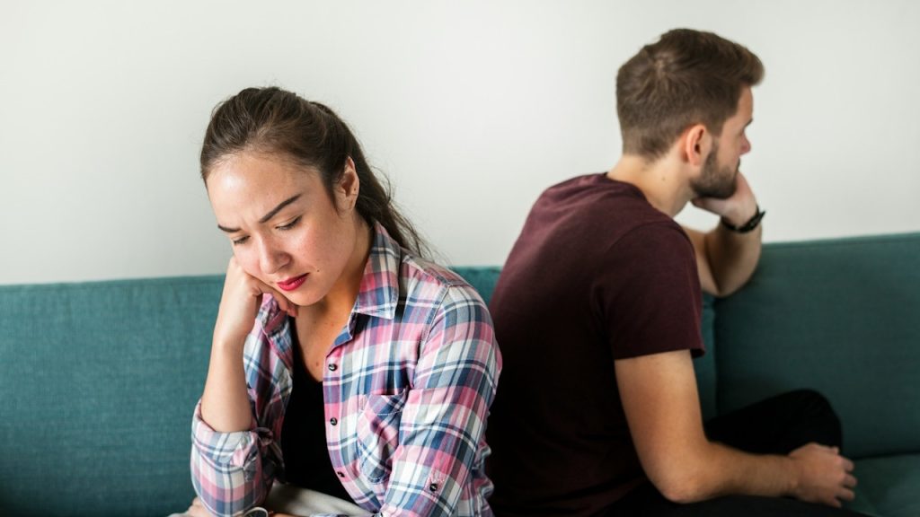 An unhappy couple sitting on a couch with their faces turned away.