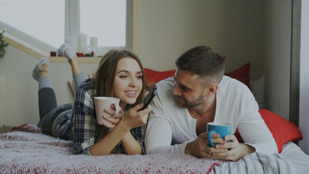 A couple relaxing on the bed with cups of coffee.