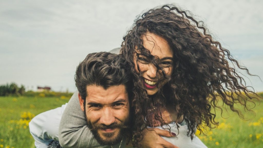 A woman riding on a man's back on a green field.