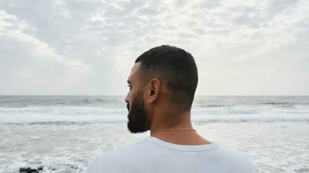 A man standing on the beach looking at the ocean.