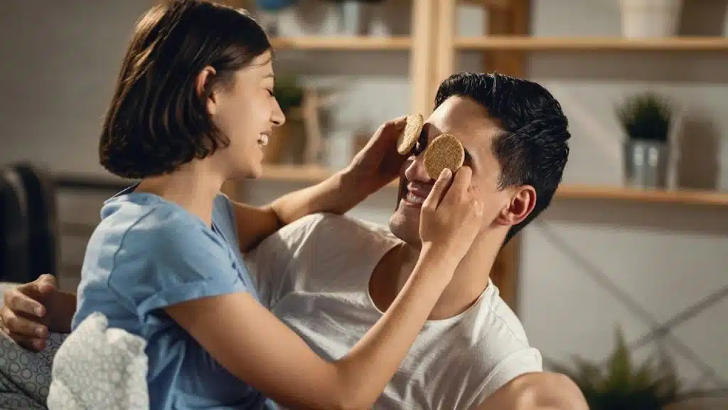 A woman is putting cookies on the eyes of the man, and both are laughing.