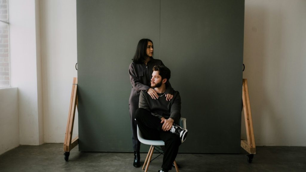 A man is sitting on a chair while a woman is standing behind her.