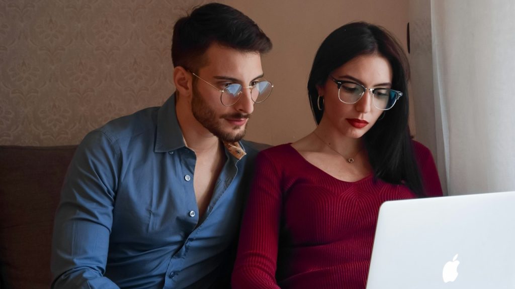 A couple wearing glasses looking at a laptop screen.
