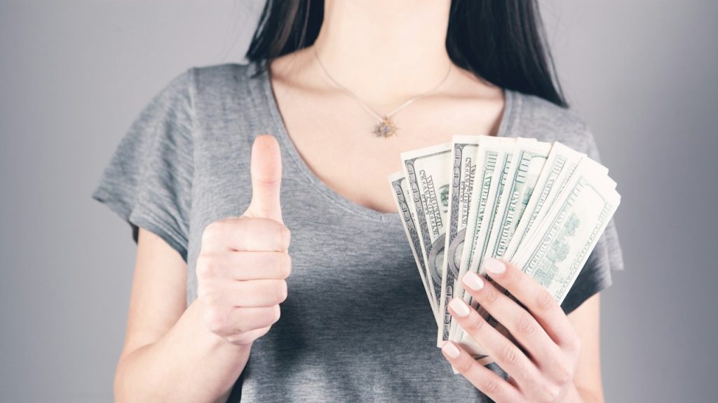 A woman holding money in one hand and making a thumbs-up gesture with the other.