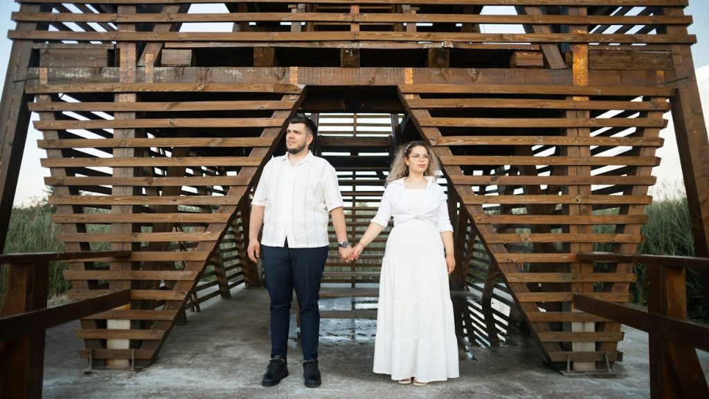 A couple holding hands and looking in opposite directions while standing on a bridge.