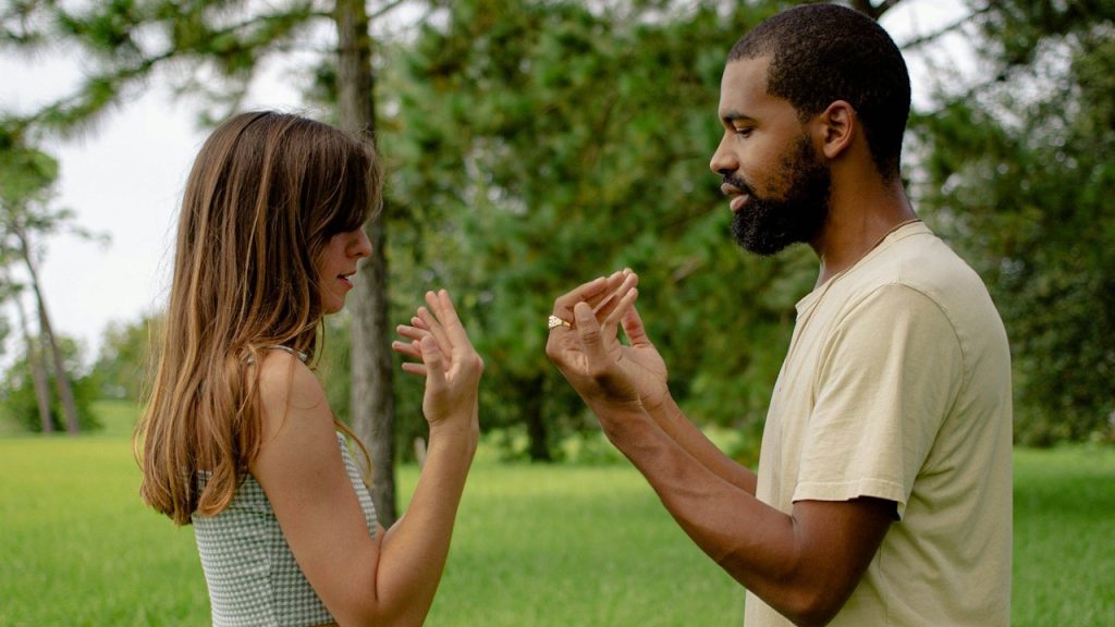 A man and a woman pointing hands at themselves.