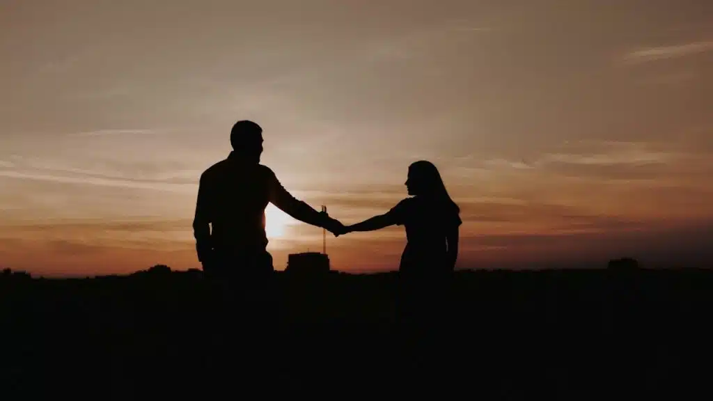 Silhouette of a couple holding hands against a sunset or sunrise.