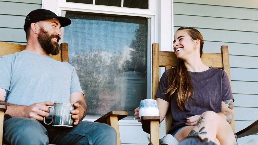 A couple smiling while having coffee on a porch.