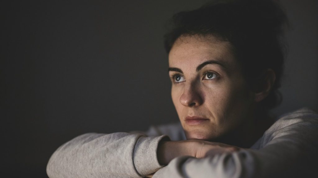 A woman rests her chin on her crossed arms, looking off into the distance with a somber and pensive expression.