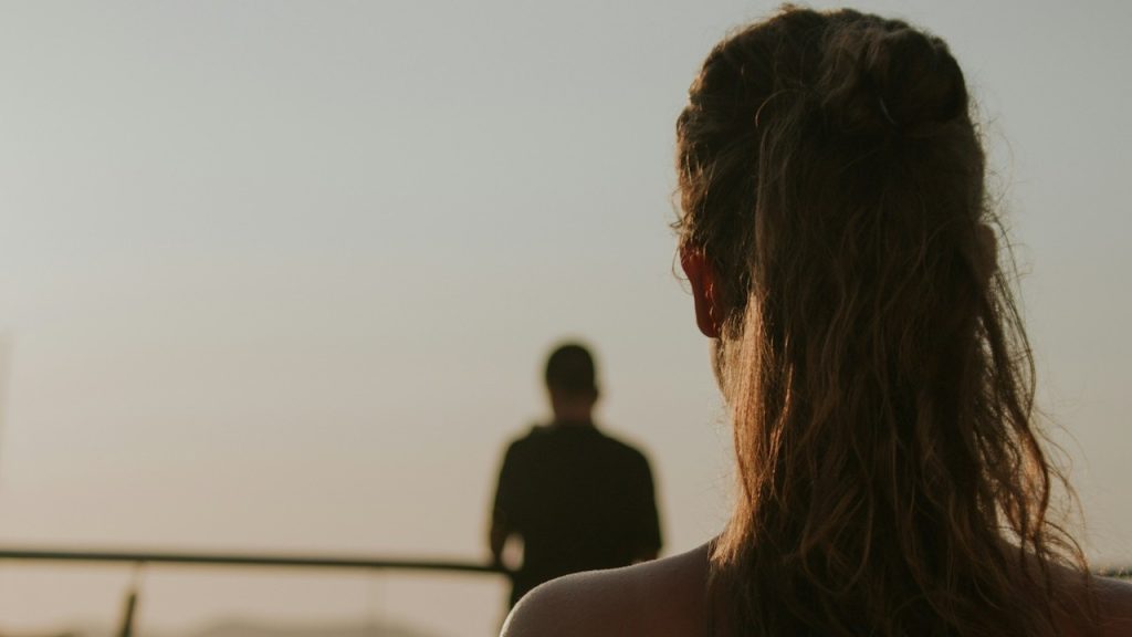 A woman is standing behind a man at the beach.