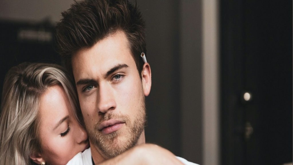 A woman is hugging a man from behind who is being sad.