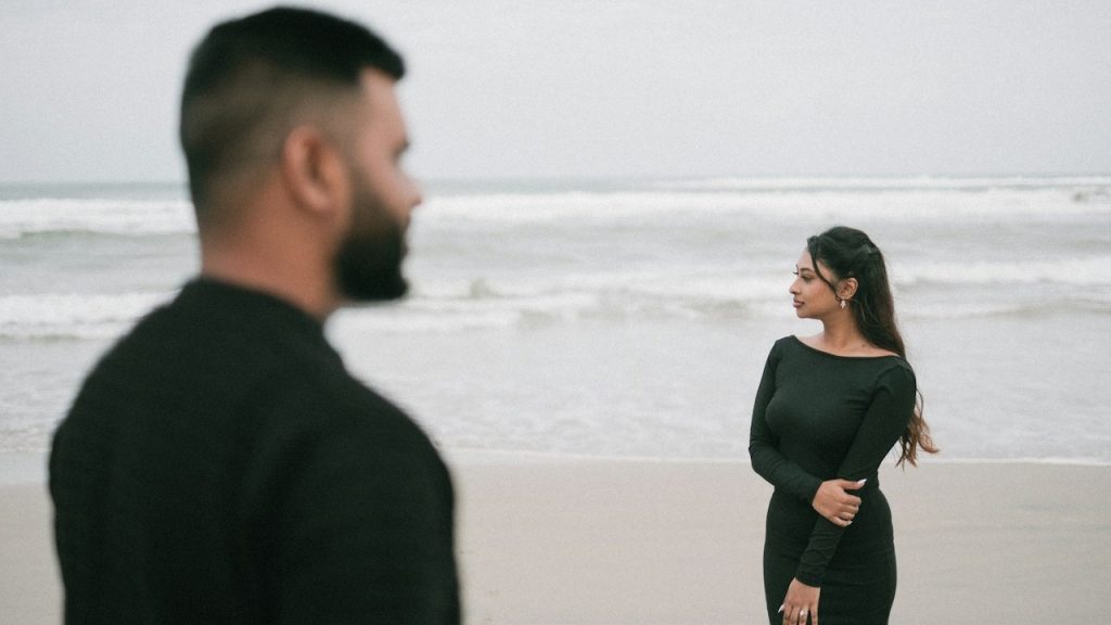 A couple wearing black dresses are standing on the beach.