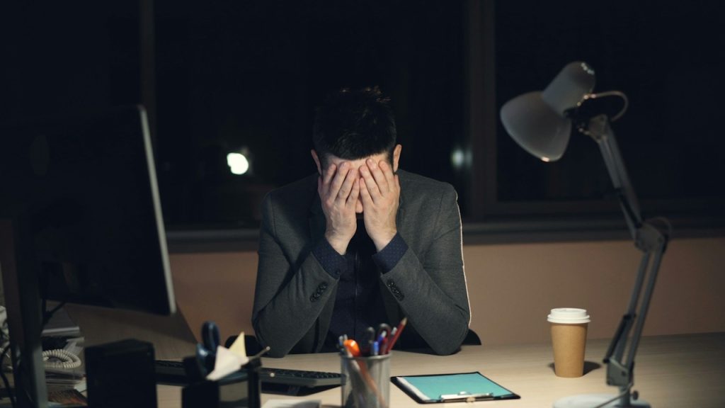 A distressed man sitting at a table, covering his face with his hands