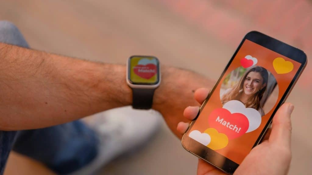 A person with a smartphone and a smartwatch with screens showing a perfect match with a picture of a woman.