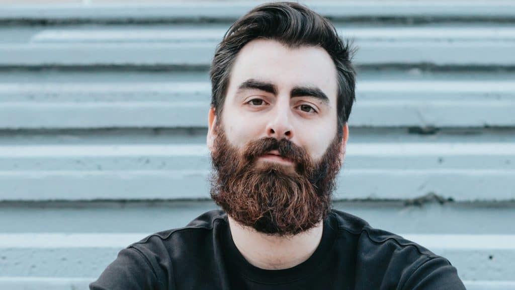 A bearded man looking at the camera with a inscrutable expression.