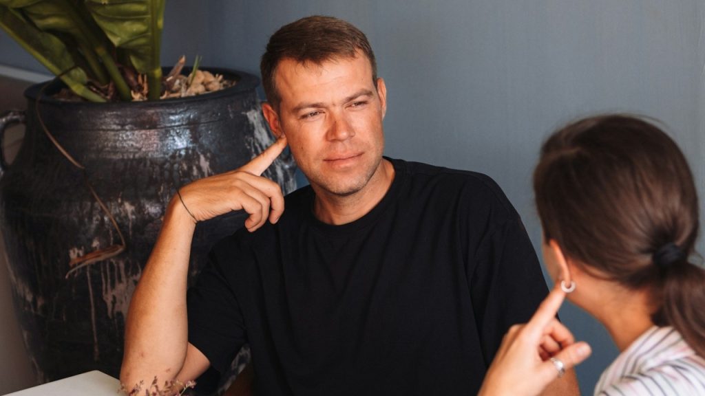 A man listening to a woman speak while they both hold their fingers on their cheeks.