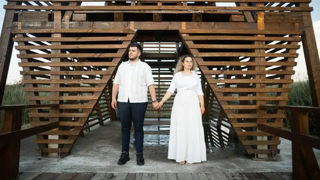 A couple holds hands under a wooden structure.
