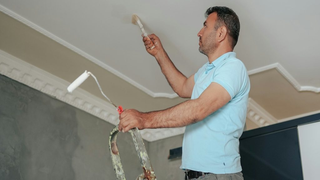 A man standing on a ladder is painting his room.