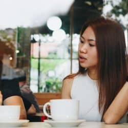 A man looking at his phone while a woman sitting across from him at a cafe table is talking and gesturing with her hand.
