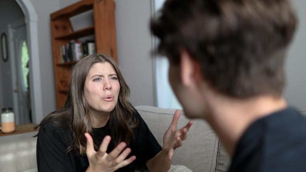 An angry woman sitting on a couch talking to a man.
