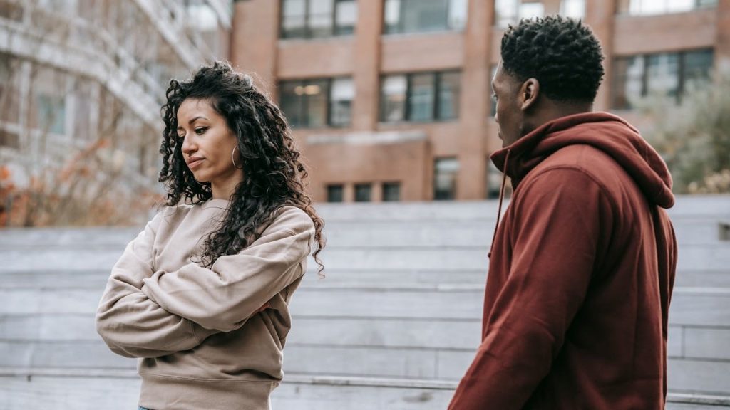 A woman with her arms crossed looking away from a man standing nearby on some steps.