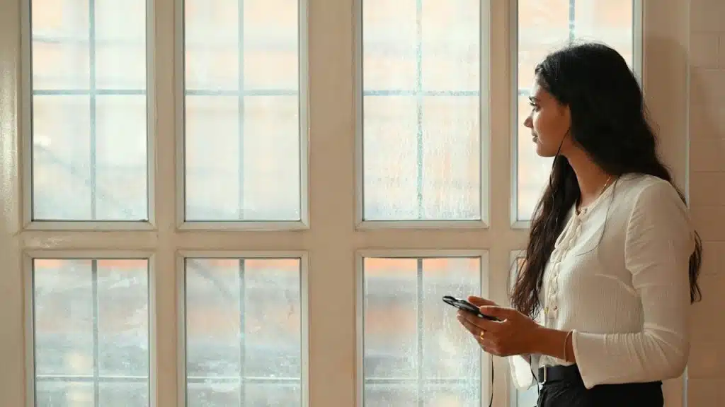 A woman holding a phone is standing in front of a huge window.