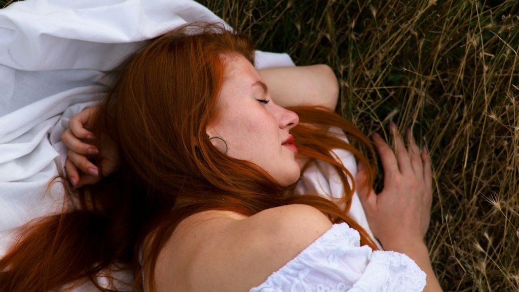A woman lying on the grass with her eyes closed.