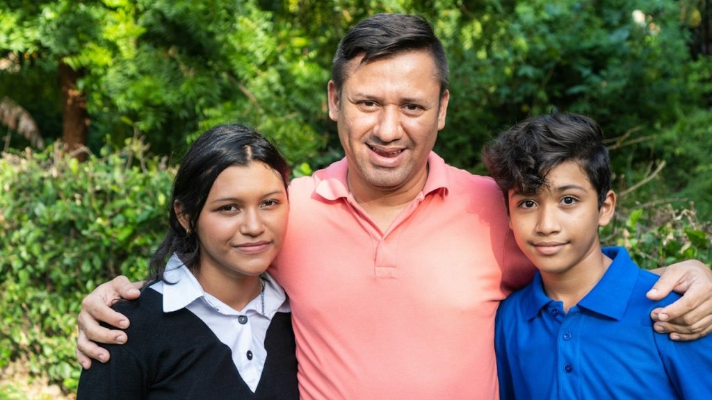 A man holdingn his kids close to him with his arms around their shoulders.