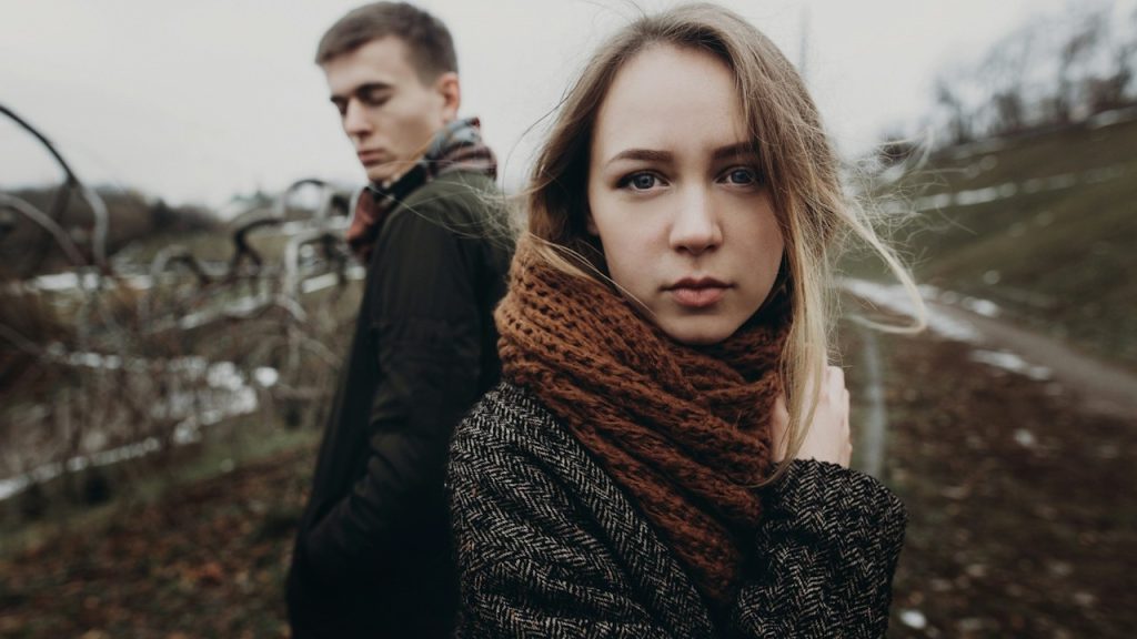 A man staring at a woman over his shoulder as they stand outdoors.