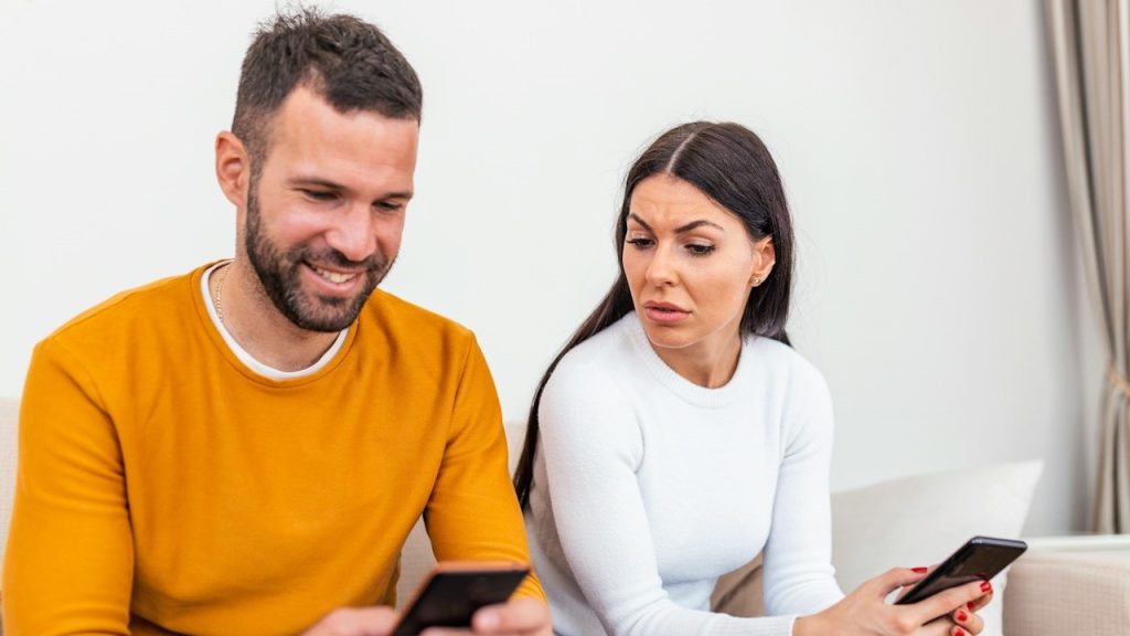 A worried woman sitting next to him, trying to peek at the screen.