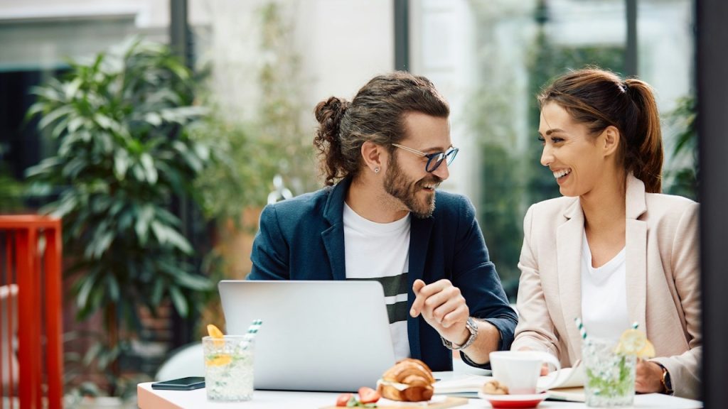 A happy man and his female coworker communicating while working on a computer in a cafe.