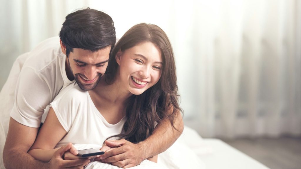 A couple laughing while looking at a mobile screen.