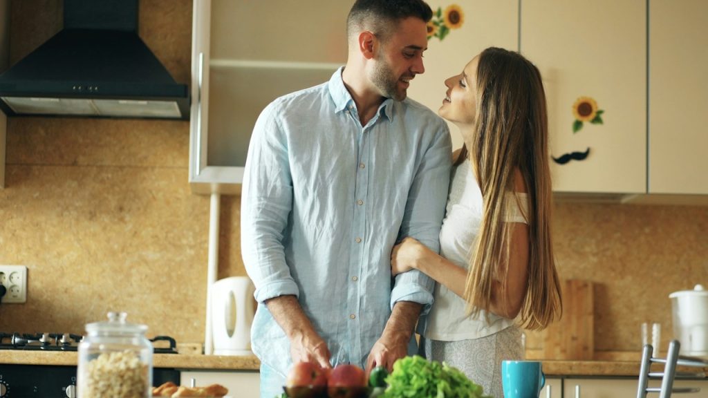 A woman holding arm of her husband while he is preparing meal in the kitchen.