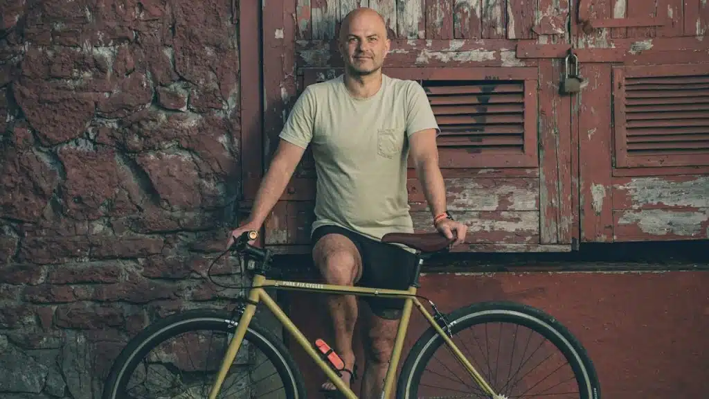 A man with a bicycle leaning against a weathered red door.