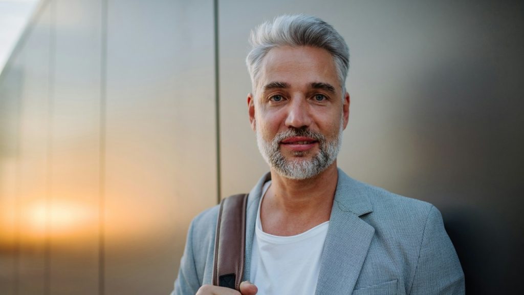 A mature, relaxed businessman leaning on a street wall and looking at the camera.