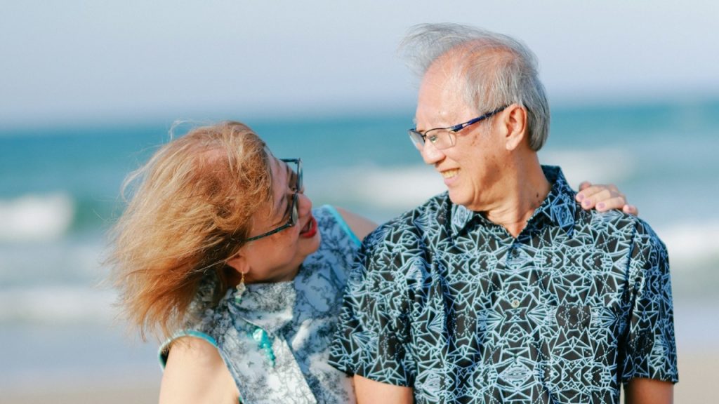 Elderly couple embracing on a sandy beach.