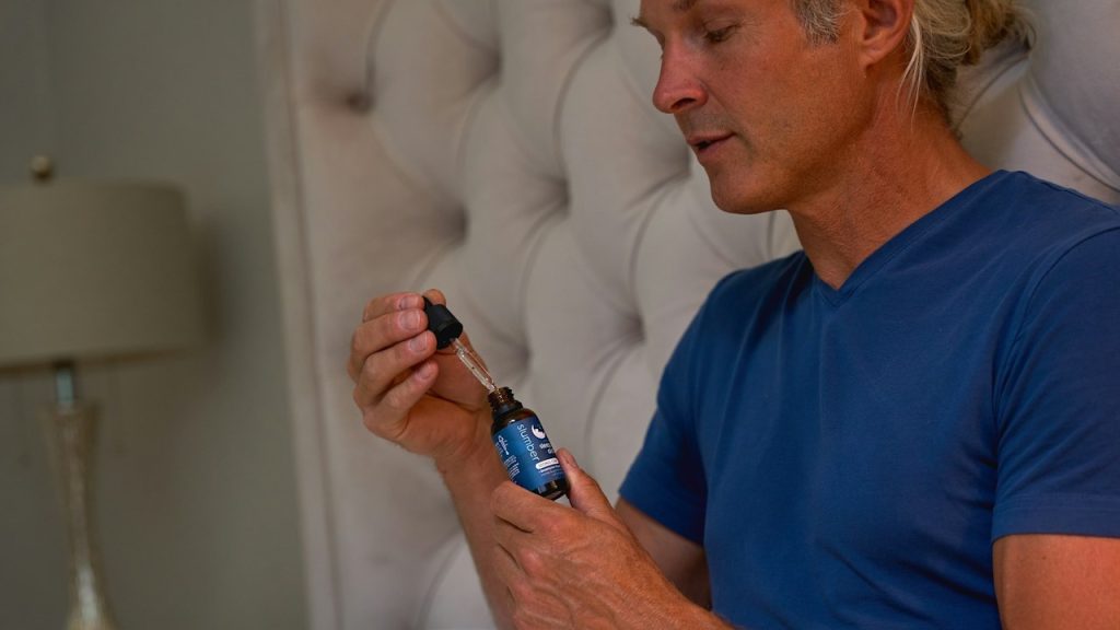 A man in a blue shirt holding a small bottle of drops that helps in sleeping.