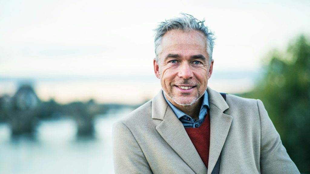 A mature, handsome businessman standing by the Vltava River in the city.